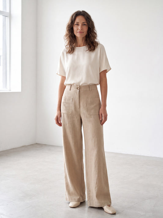 Three pairs of textured linen trousers in raw linen, dark coffee, and black hanging on a rack.