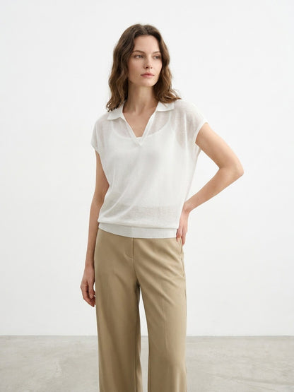 Woman modeling a white short-sleeved collared knit top.