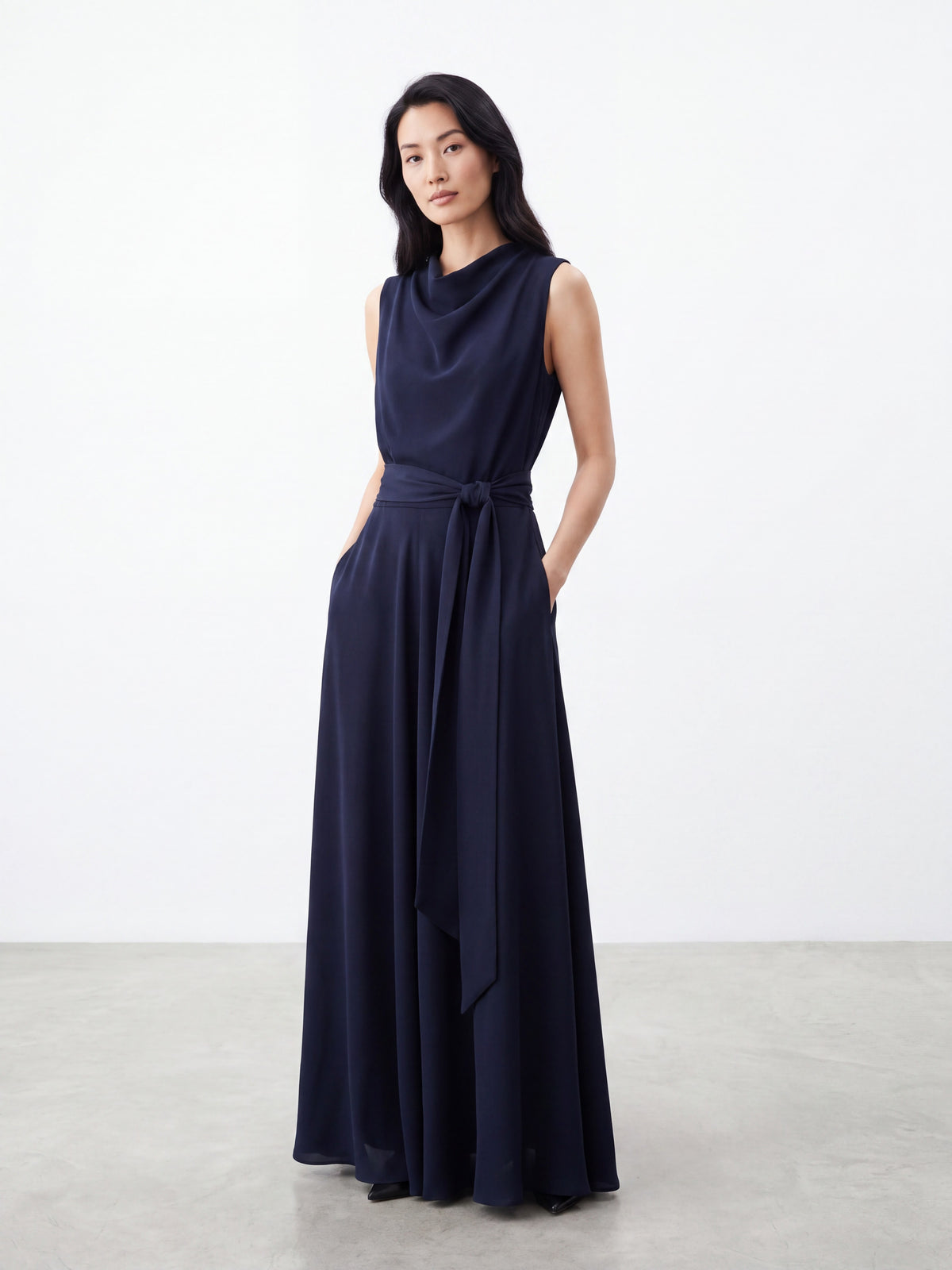 Model wearing dark navy blue draped neck sleeveless dress with tie waist