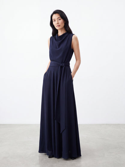 Model wearing dark navy blue draped neck sleeveless dress with tie waist