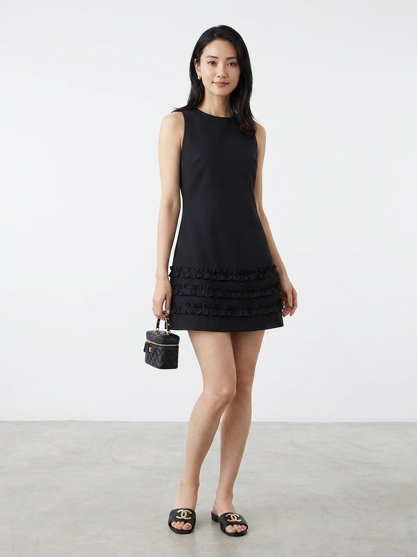 Model wearing black sleeveless ruffle hem mini dress holding a bag