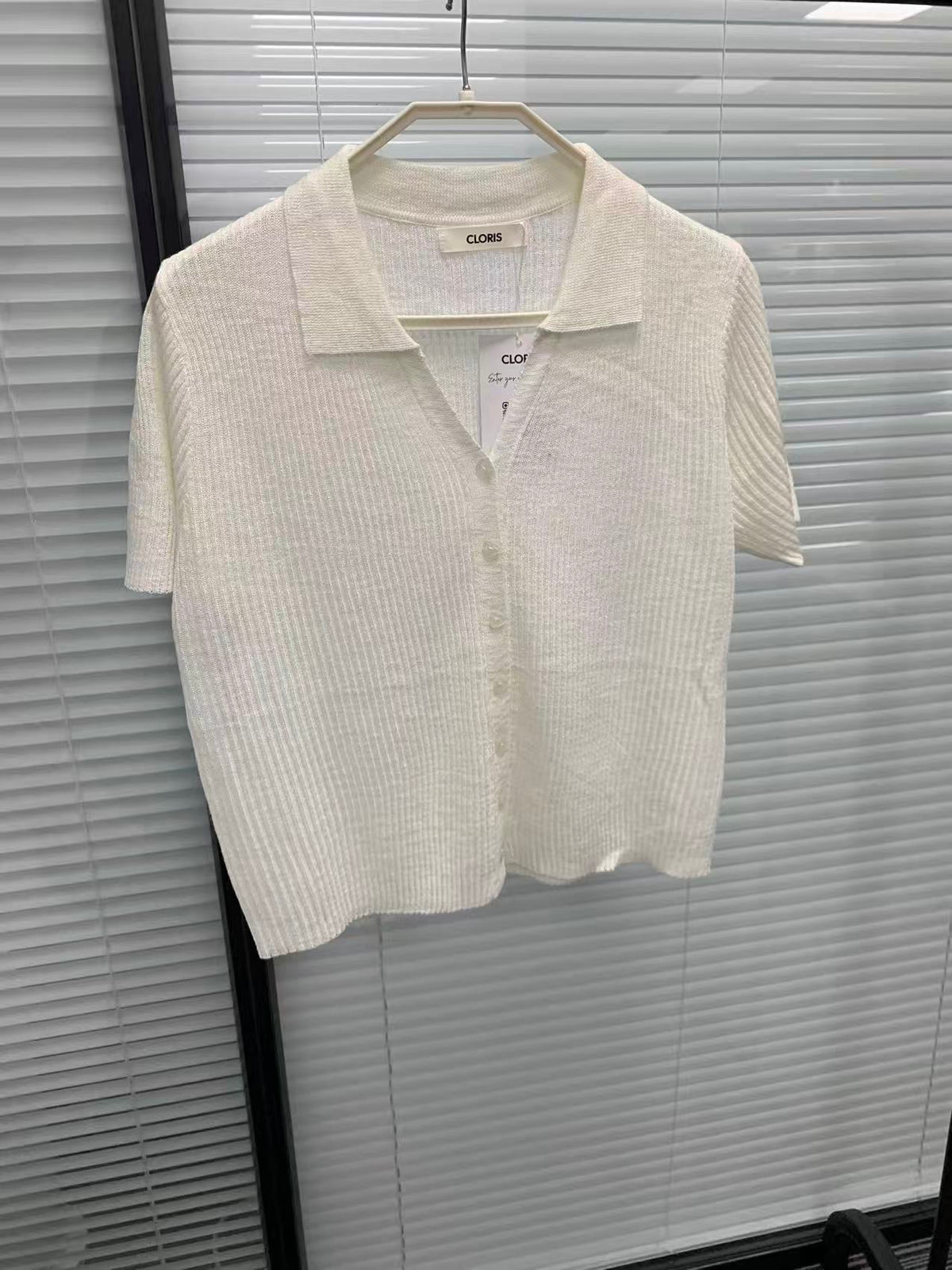 White short-sleeve ribbed knit polo shirt with button-down front hanging on a hanger