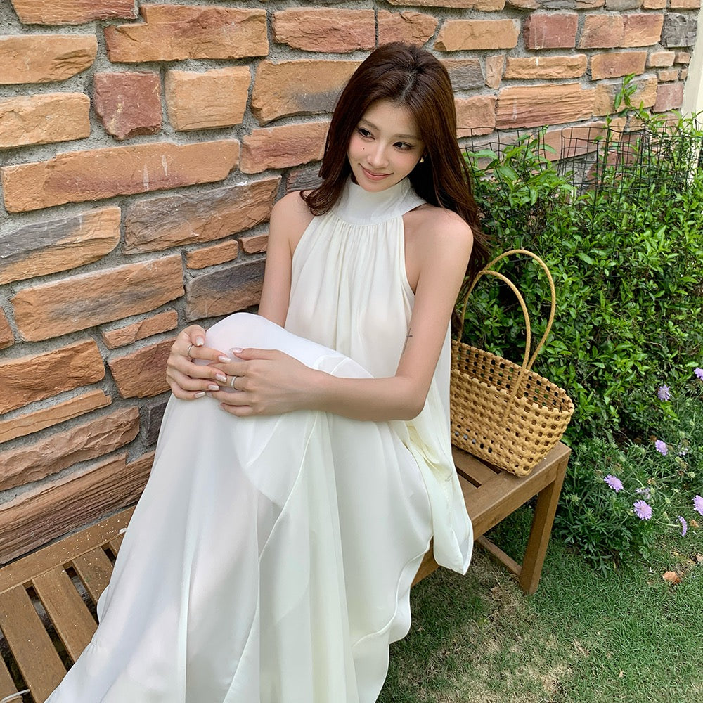 Woman wearing a white halter neck sleeveless chiffon top and A-line skirt set sitting on a bench