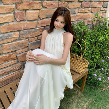 Woman wearing a white halter neck sleeveless chiffon top and A-line skirt set sitting on a bench