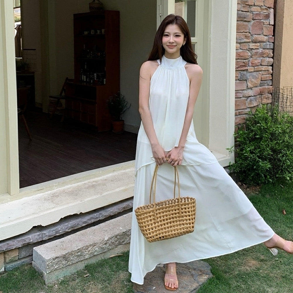 Woman in a white sleeveless maxi dress set holding a woven basket bag