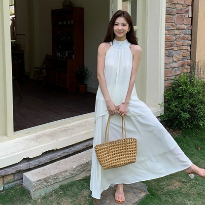 Woman in a white sleeveless maxi dress set holding a woven basket bag