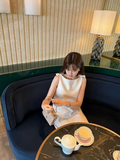 Woman sitting in a cafe wearing the elegant off-white sleeveless dress.