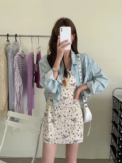 Woman taking a mirror selfie wearing a light blue denim jacket over a floral mini dress