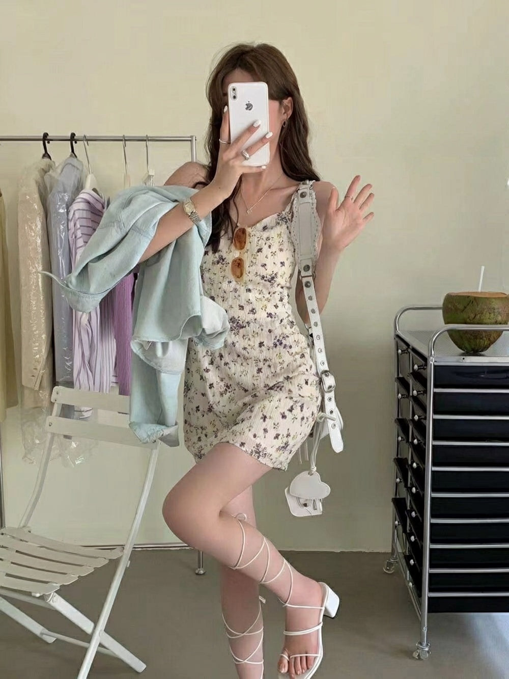 Woman taking a mirror selfie wearing a floral mini dress and holding a light blue denim jacket
