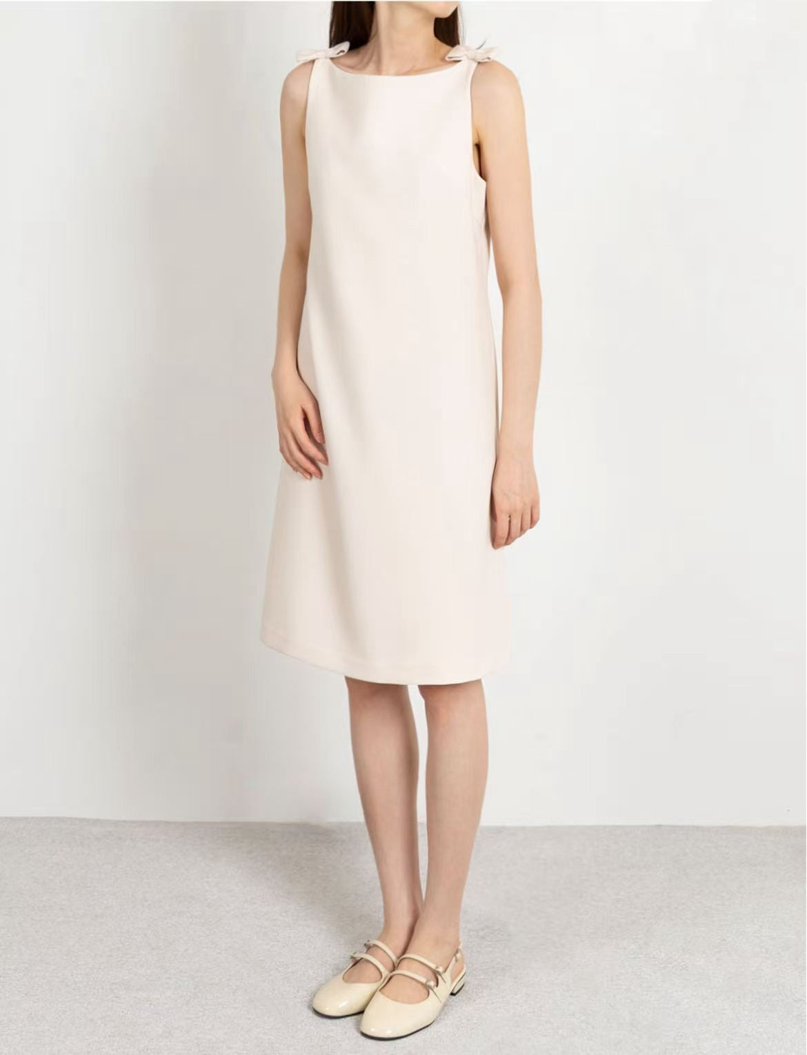 Full-length view of the model in the off-white knee-length sleeveless dress.