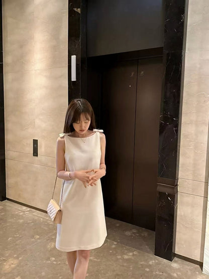 Woman wearing an elegant off-white sleeveless dress with shoulder bows in front of an elevator.