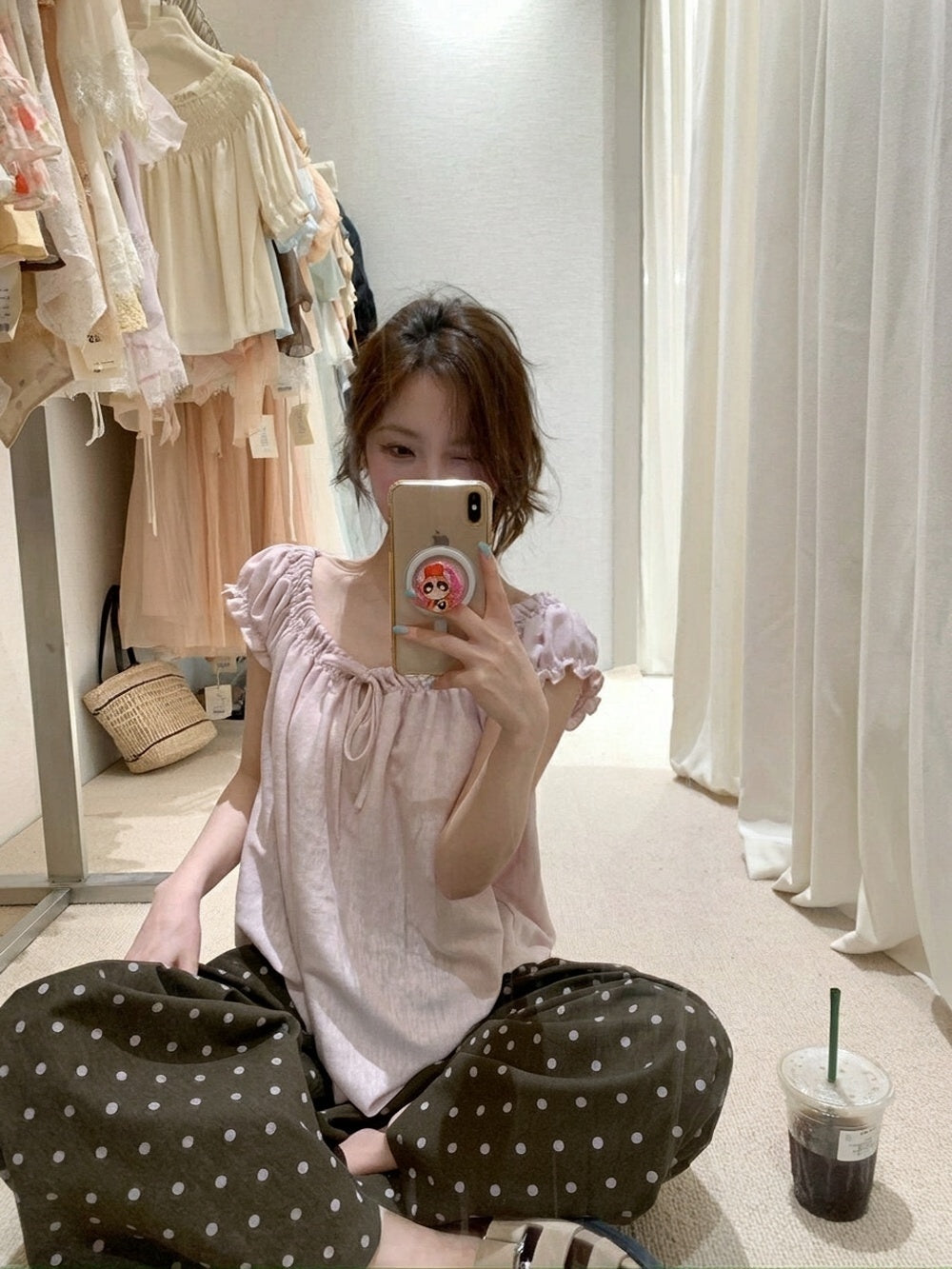 Woman sitting on the floor taking a mirror selfie in a pink gathered short sleeve top