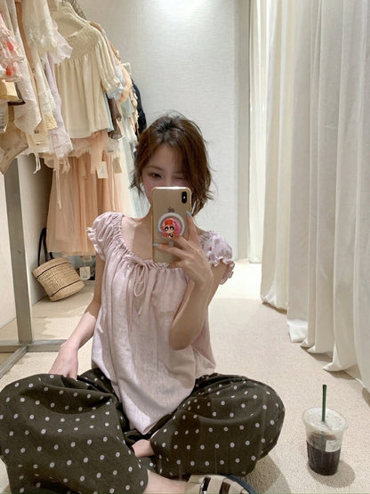 Woman sitting on the floor taking a mirror selfie in a pink gathered short sleeve top