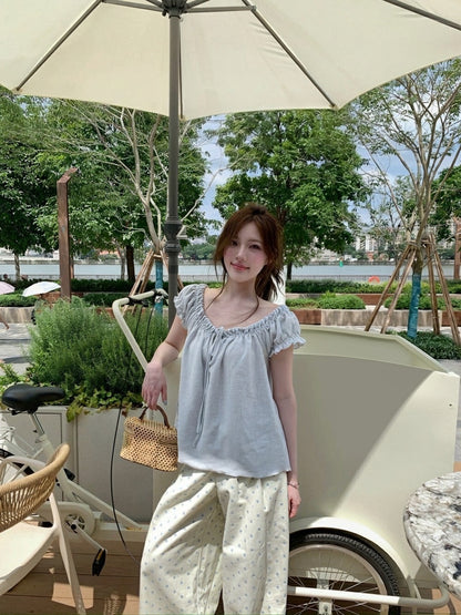 Woman standing outdoors wearing a light blue gathered tie-front short sleeve top