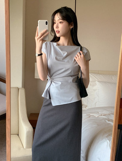 Woman wearing a light blue cowl neck tie-waist short sleeve top taking a mirror selfie.