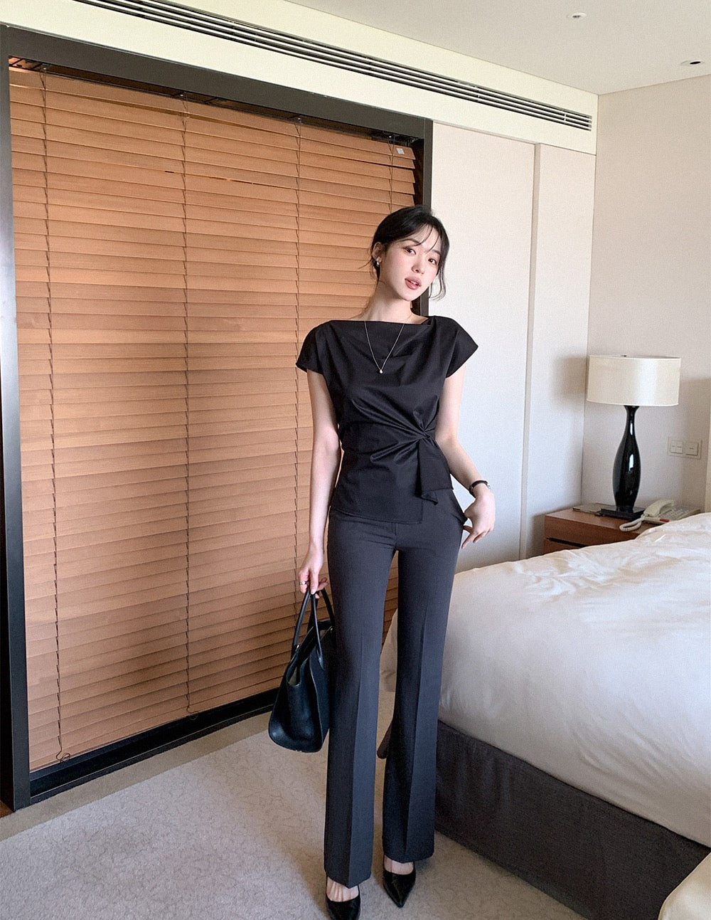 Woman wearing a black elegant draped neck top and dark trousers.