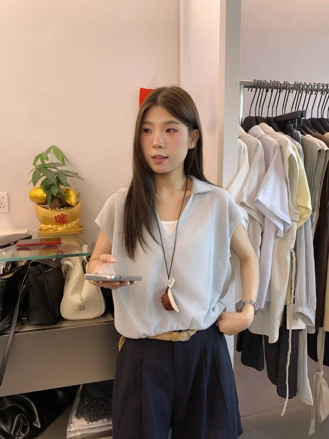 Woman modeling a light blue short-sleeved collared top with a woven belt.