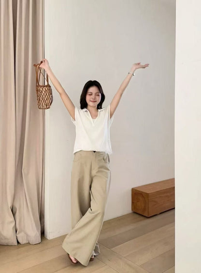 Woman in a white sleeveless collared top and beige wide-leg pants holding a bag.