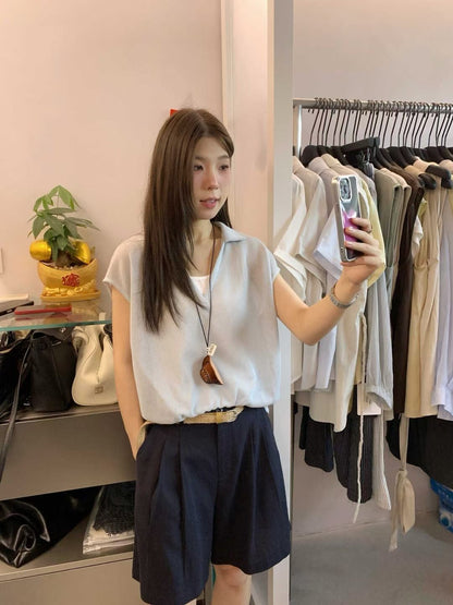 Woman taking a mirror selfie wearing a light blue collared knit top.