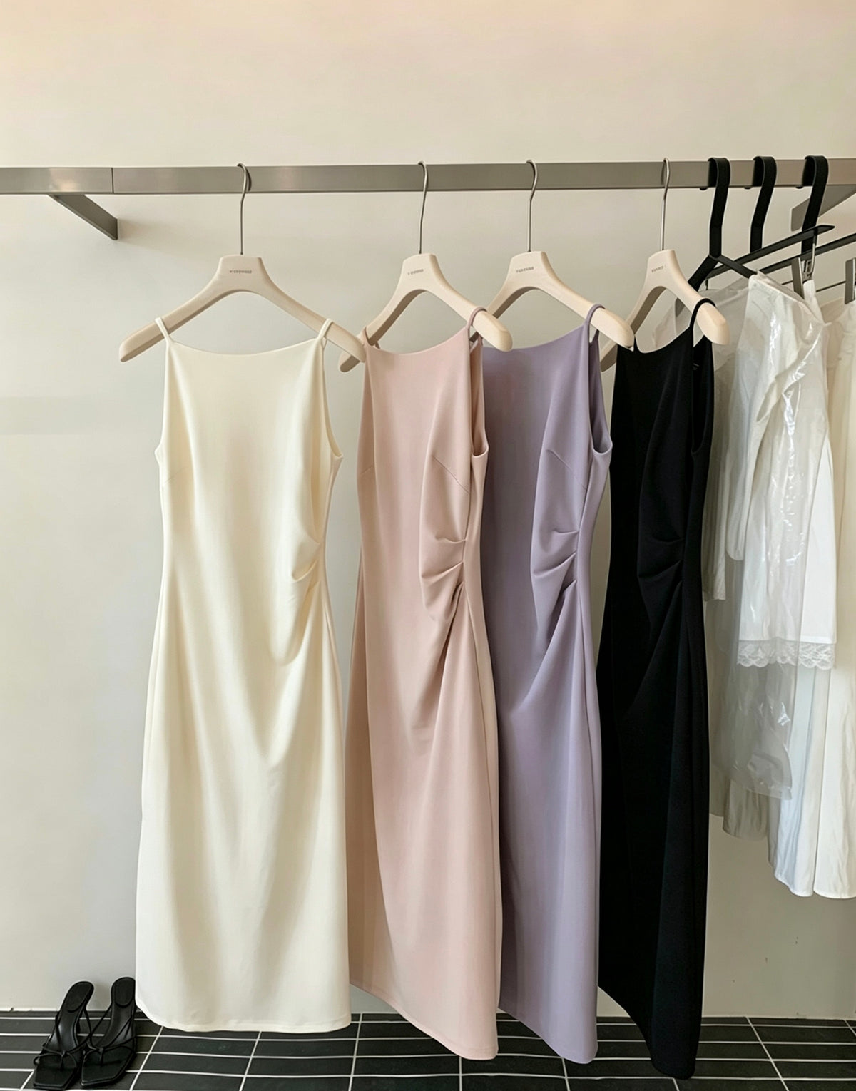 Four sleeveless dresses in white, pink, purple, and black hanging on a rack