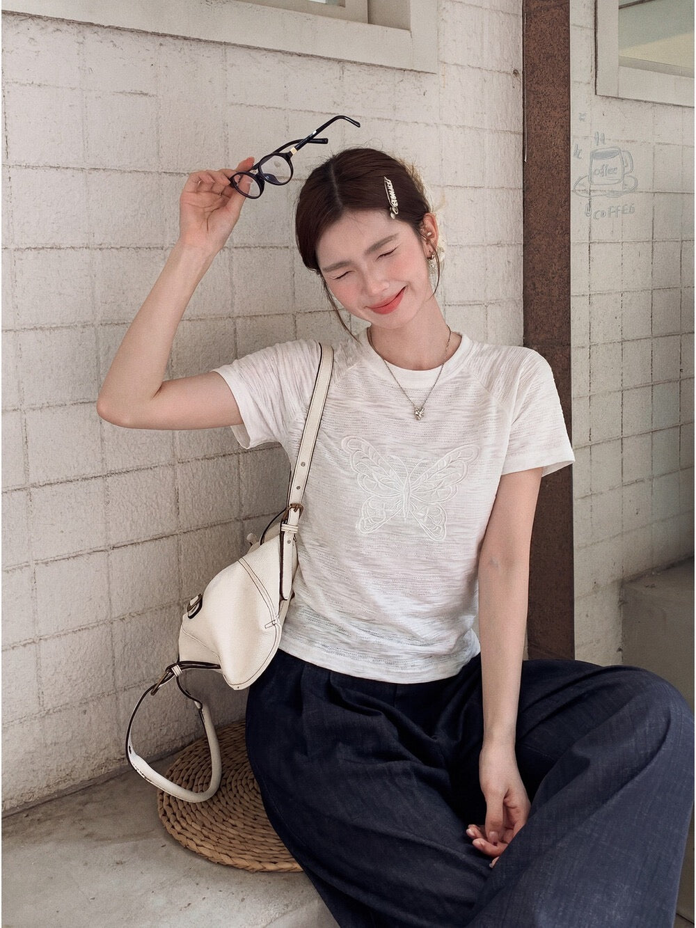 Model wearing white butterfly embroidered t-shirt holding glasses