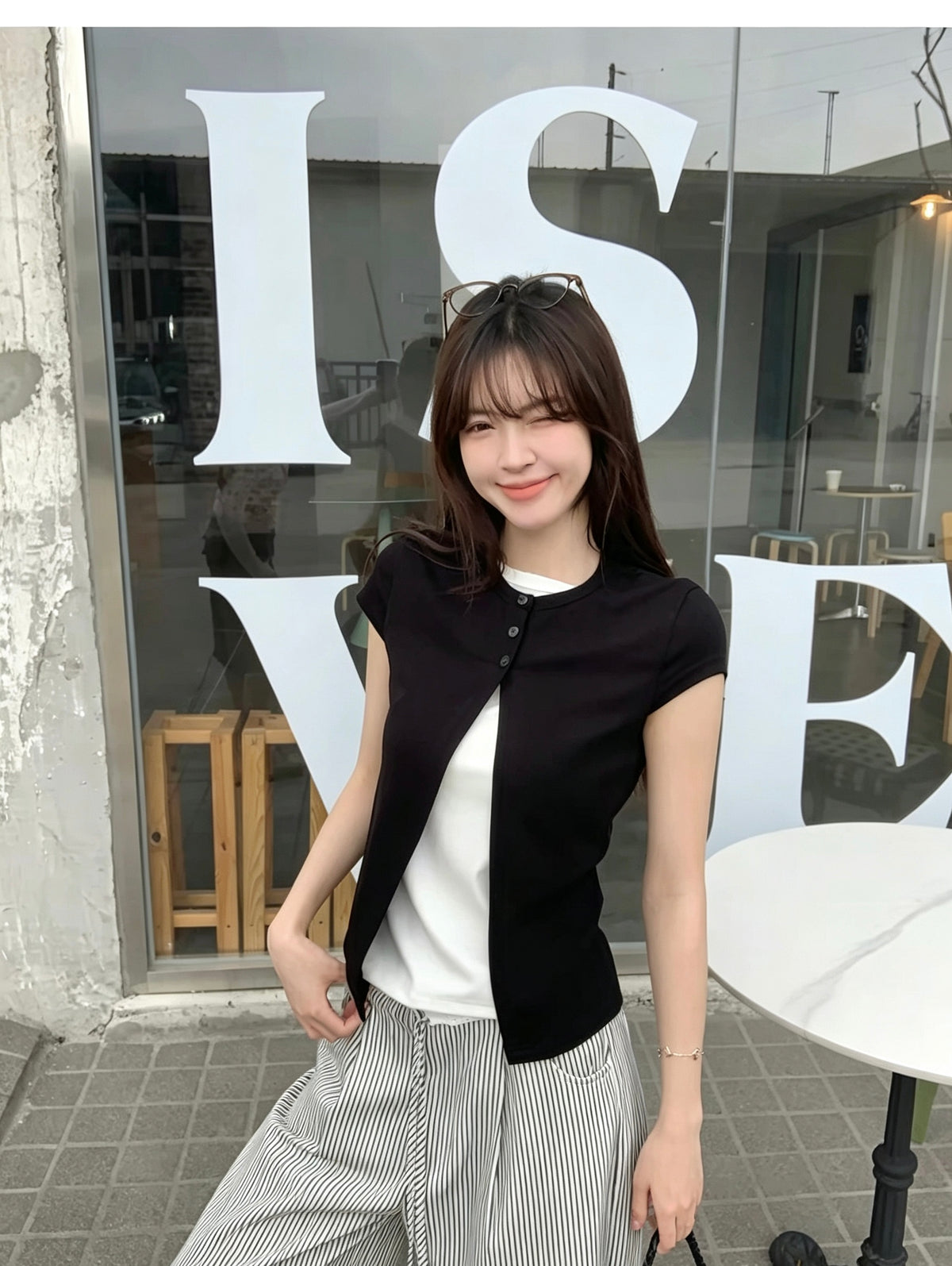 Model wearing a black faux two-piece short sleeve shirt standing in front of glass