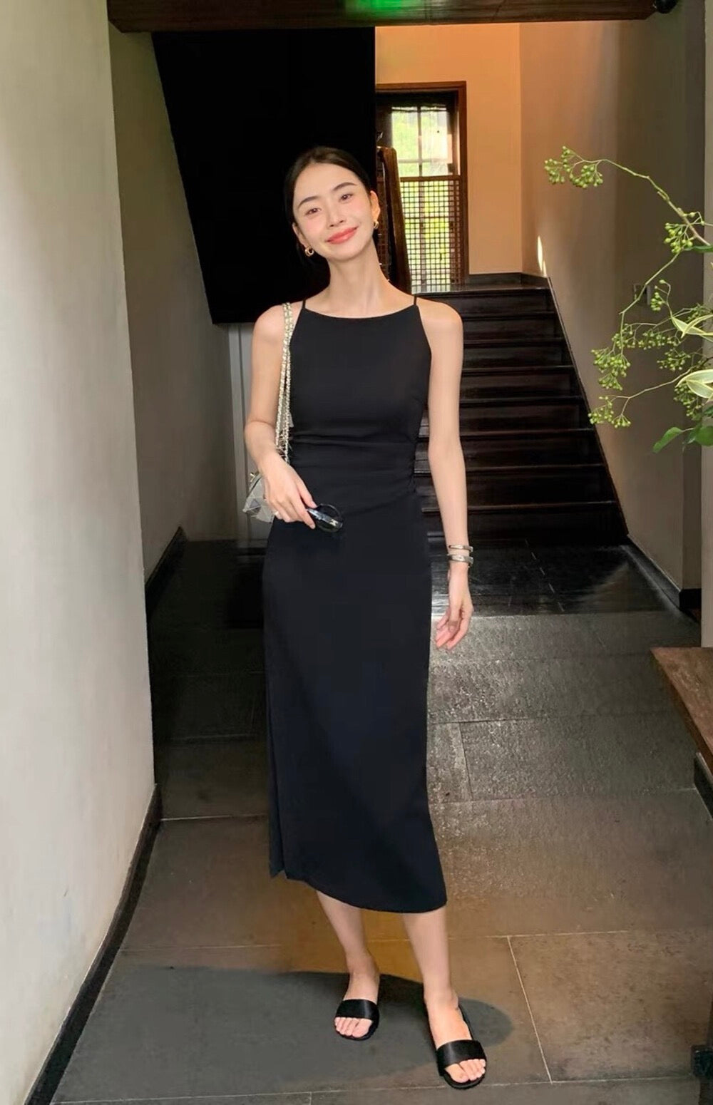 Model in a black sleeveless midi dress standing near a staircase