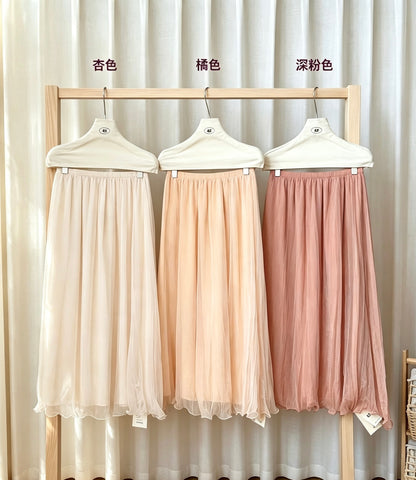 Three pearlescent mesh skirts in apricot, peach, and dark pink hanging on a rack