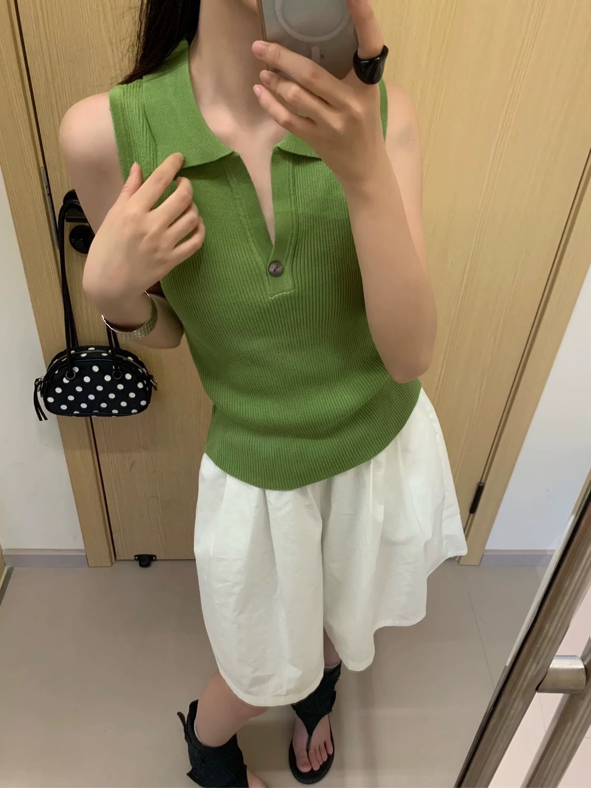 Model wearing green ribbed sleeveless polo top taking mirror selfie