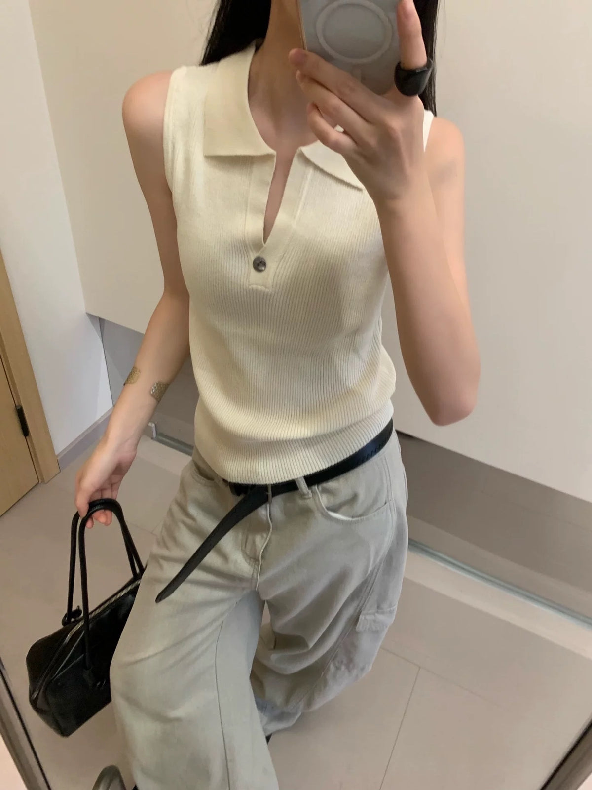 Model wearing apricot ribbed sleeveless polo top taking mirror selfie