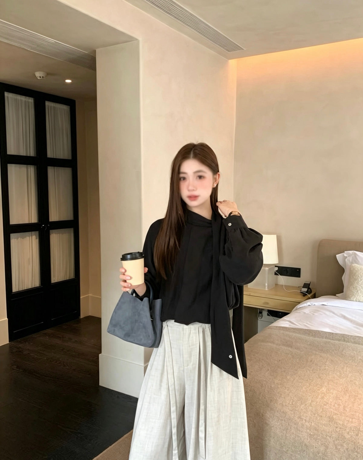 Model wearing a black two-way tie blouse holding a coffee cup.