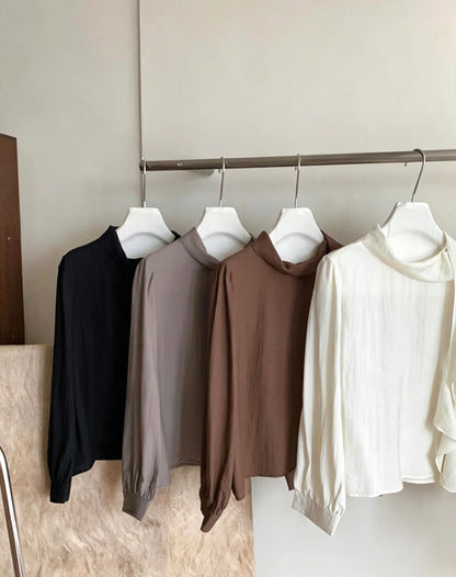 Four long-sleeve blouses in black, grey, brown, and white hanging on a rack