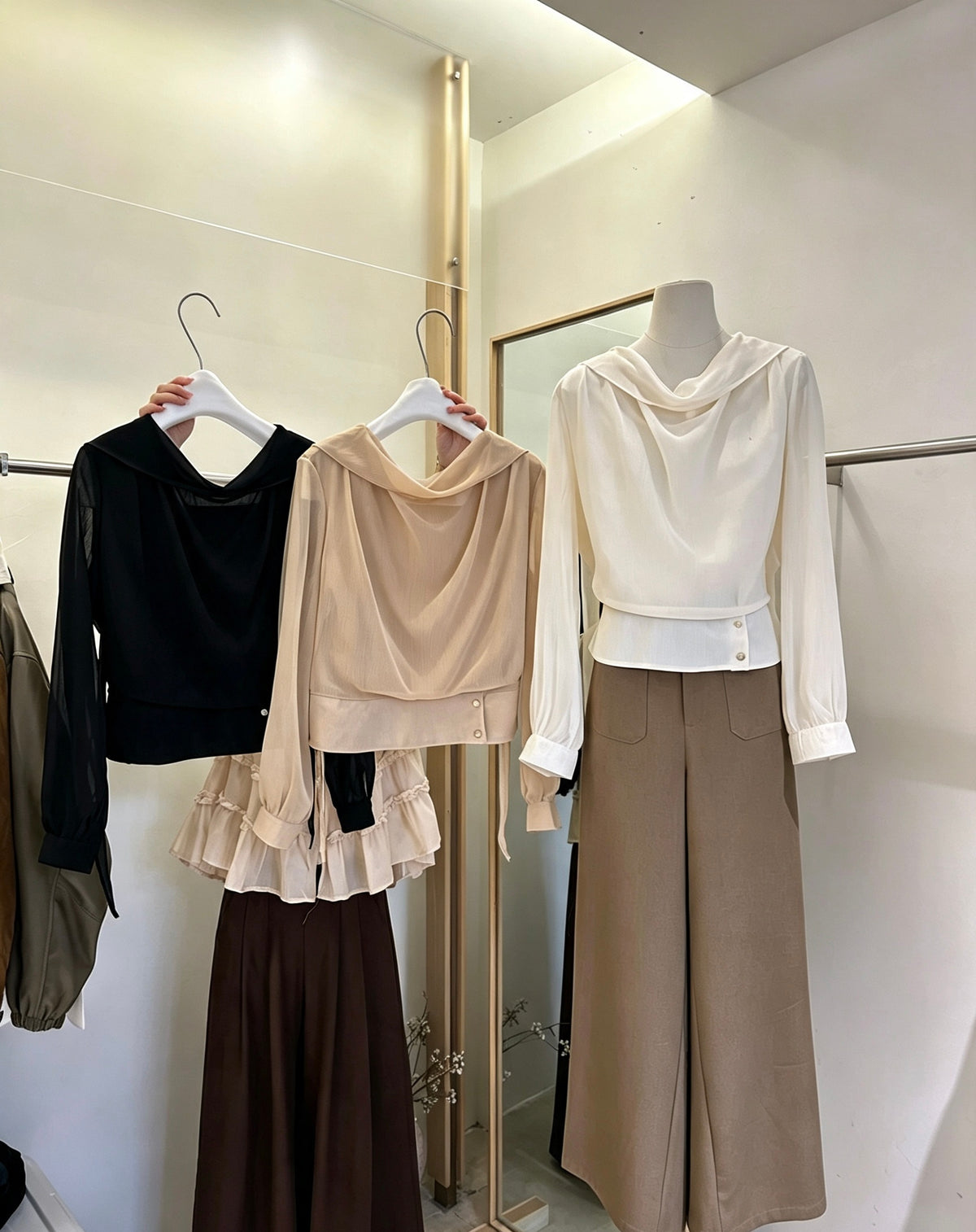 White, black, and beige draped neck tie-waist blouses on display