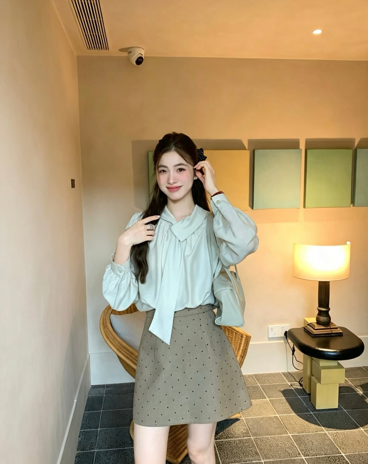 Model wearing a light khaki tie-neck blouse and a polka dot skirt