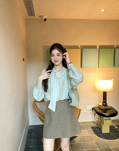 Model wearing a light khaki tie-neck blouse and a polka dot skirt