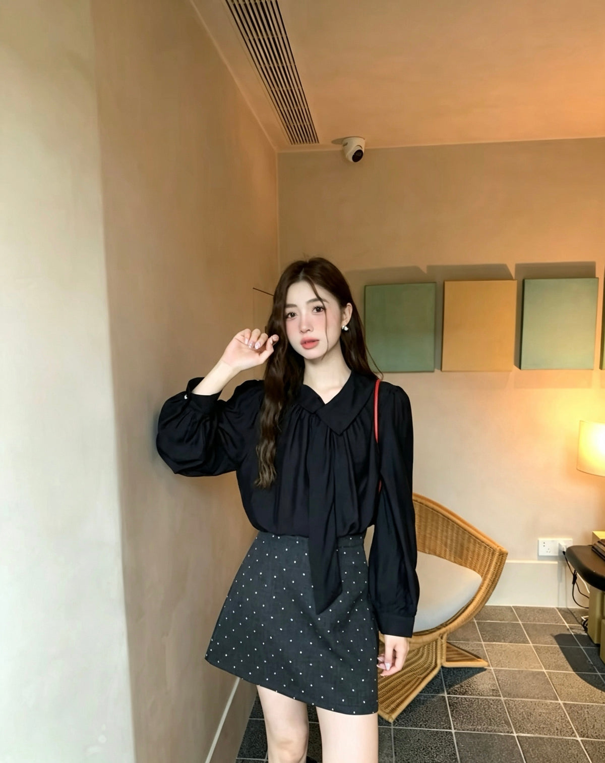 Model wearing a black long-sleeved tie-neck blouse and polka dot skirt