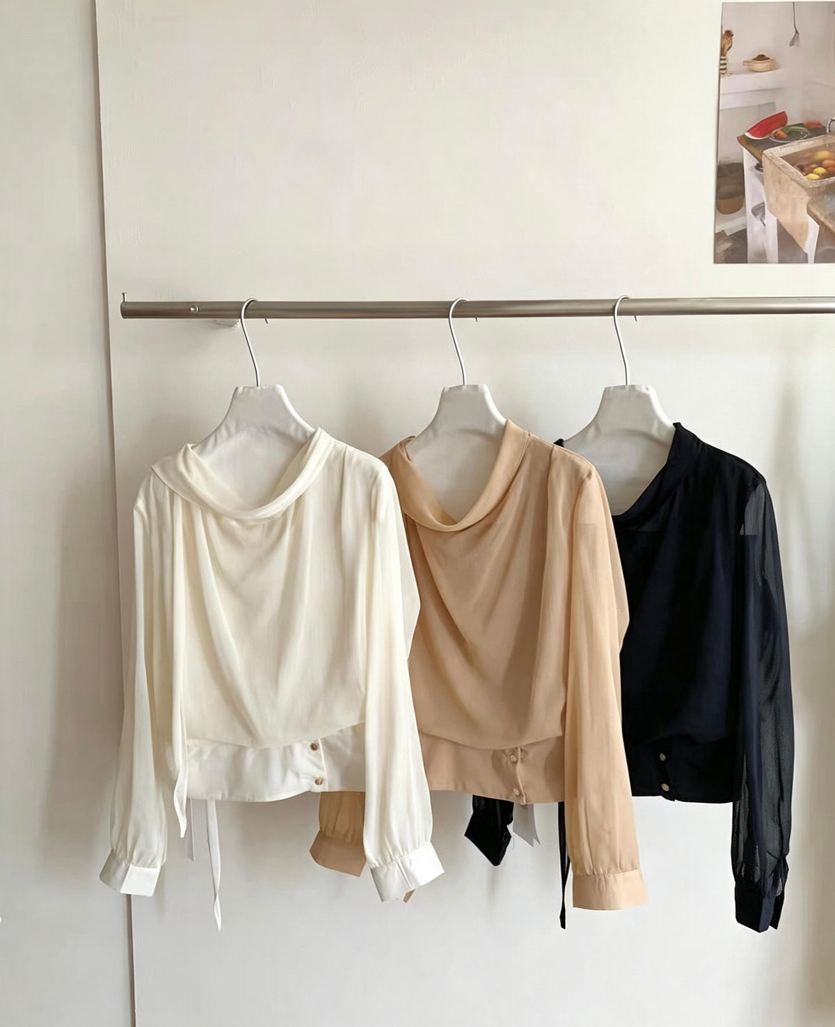 Three sheer long-sleeve draped neck blouses hanging on a rack