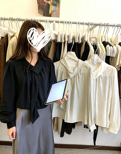 Model wearing a black tie-neck blouse holding a tablet in front of a clothing rack