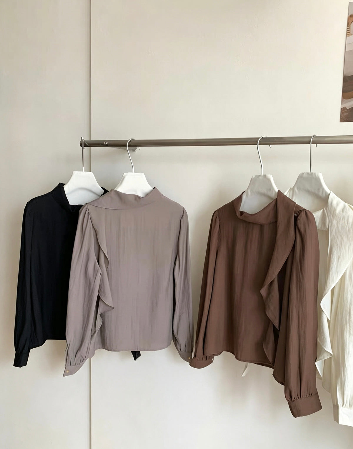 Close-up of four blouses in black, grey, brown, and white on a rack