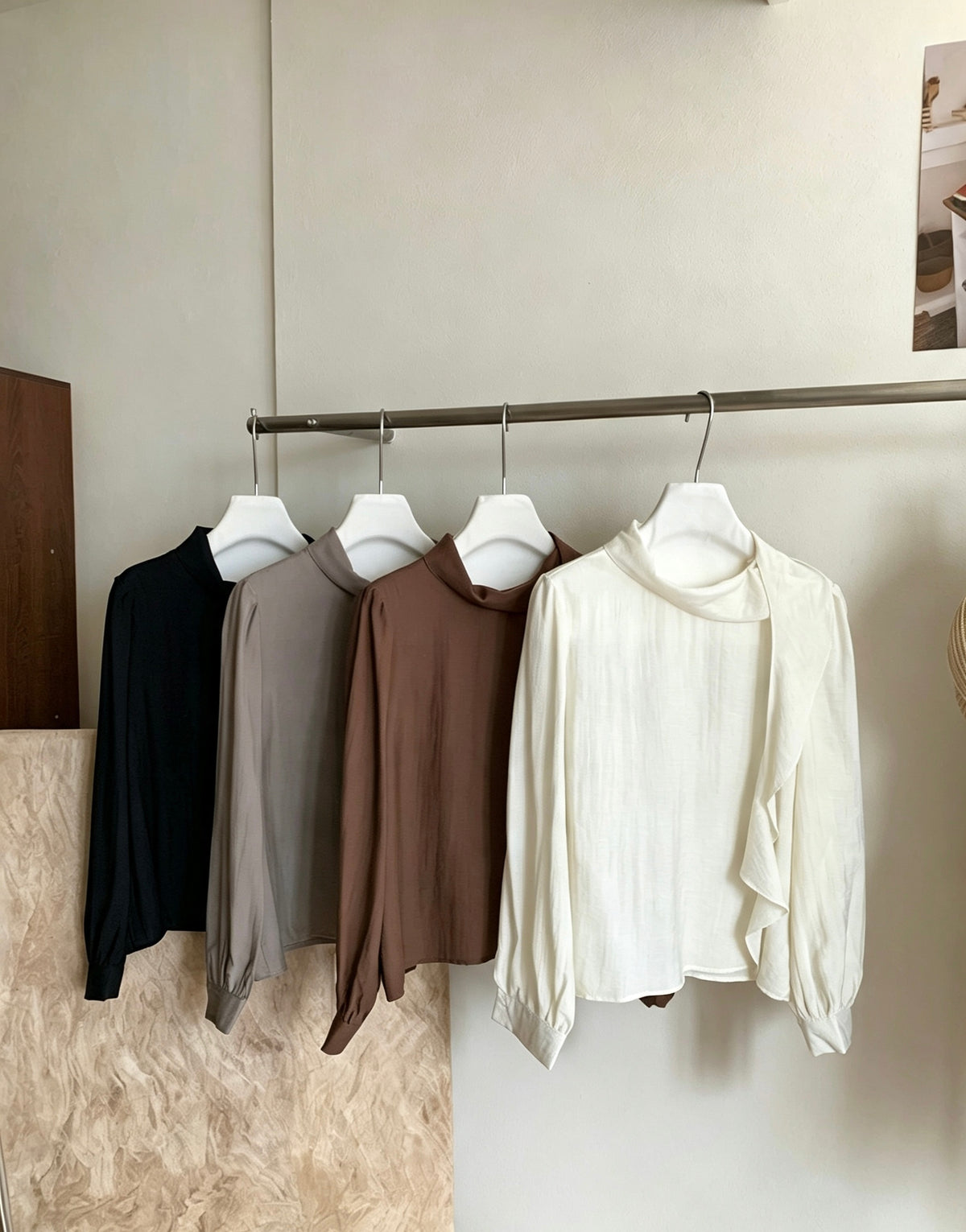 Four blouses in black, grey, brown, and white hanging on a rack