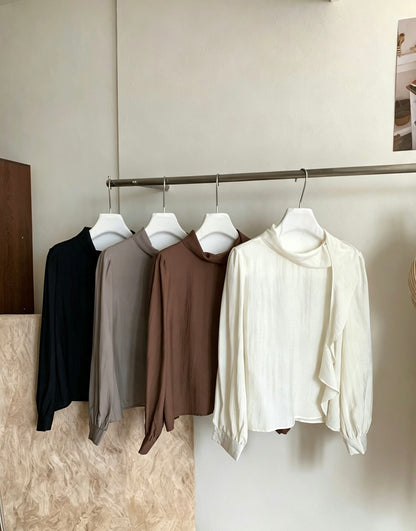 Four blouses in black, grey, brown, and white hanging on a rack