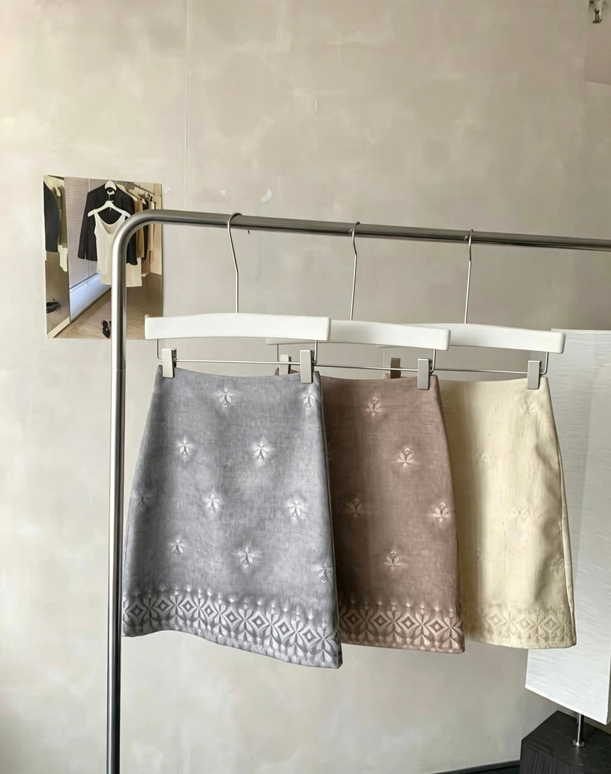 Three embroidered tie-dye vintage skirts in grey, brown, and cream hanging on a rack