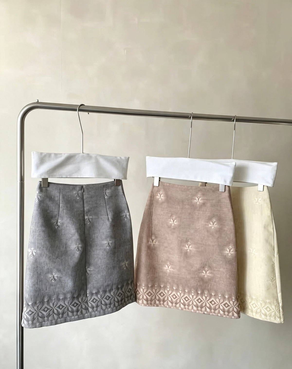 Three embroidered tie-dye vintage skirts in grey, brown, and cream hanging on a rack