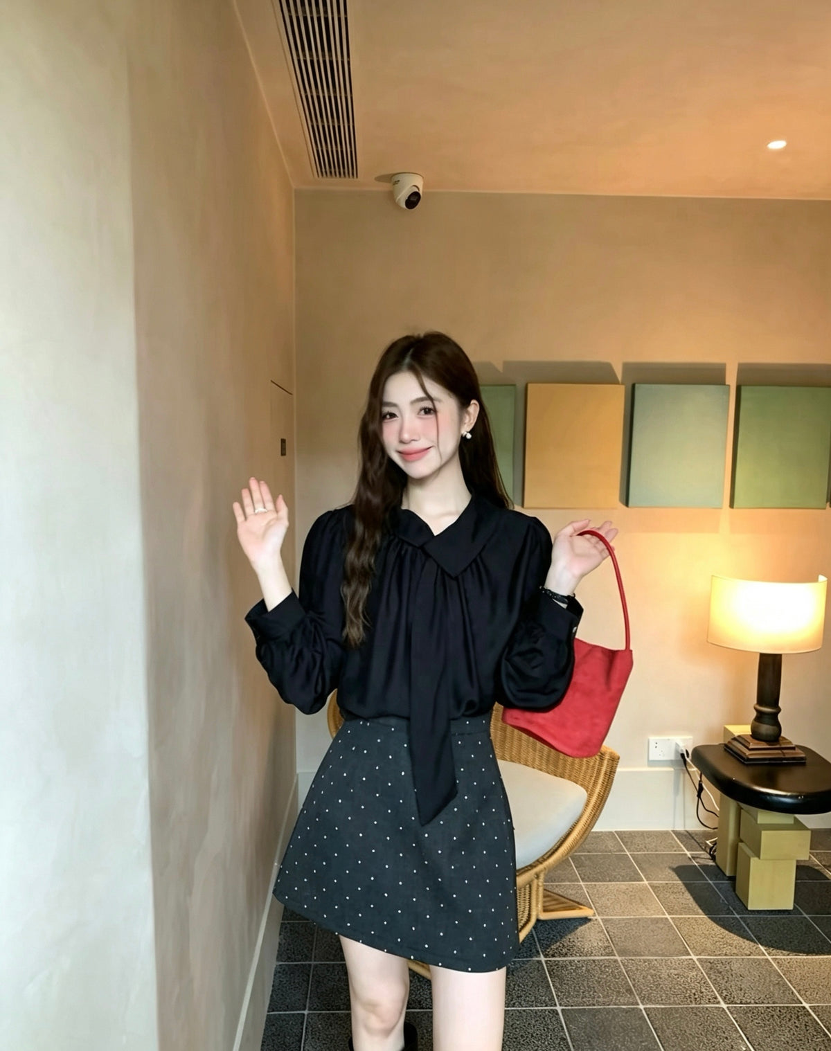 Model wearing a black tie-neck blouse holding a red handbag