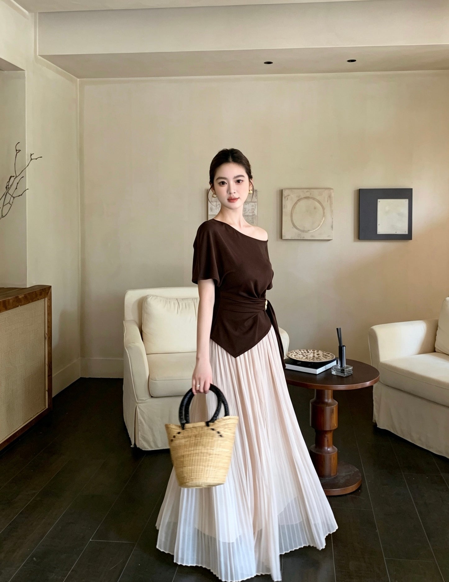 Model standing in an apricot pleated maxi skirt and brown asymmetrical top