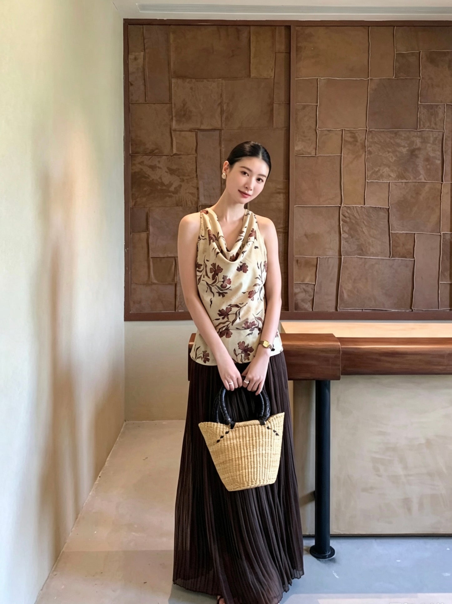 Model in a dark brown pleated maxi skirt holding a straw bag