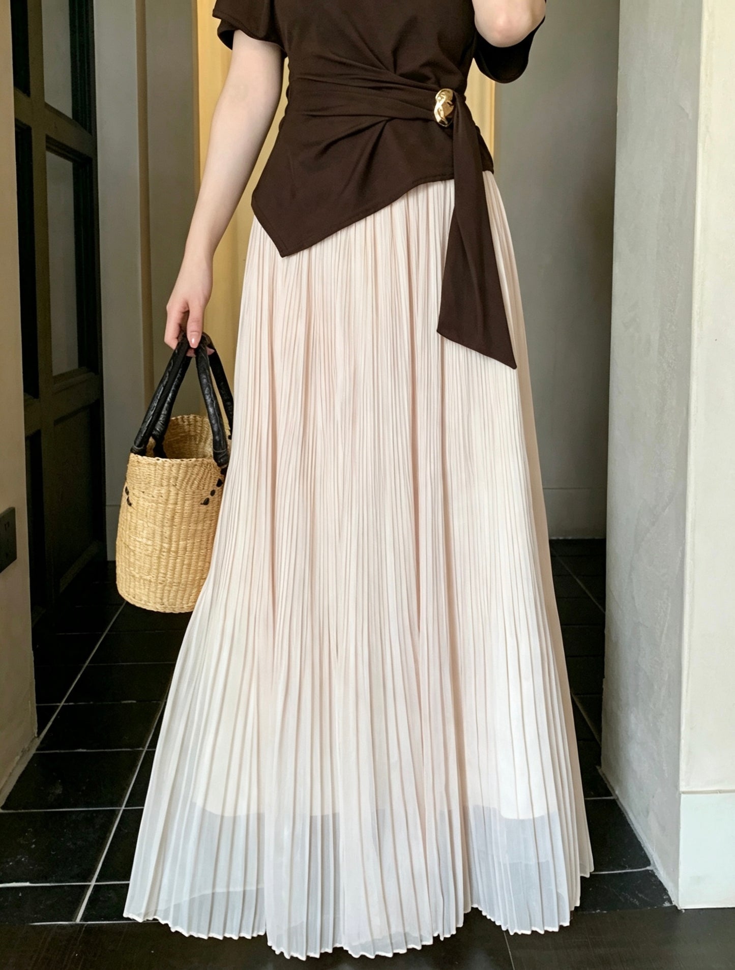 Model holding a straw bag wearing an apricot pleated maxi skirt