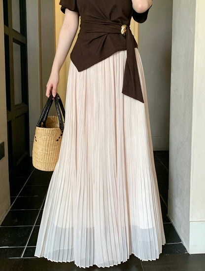 Model holding a straw bag wearing an apricot pleated maxi skirt