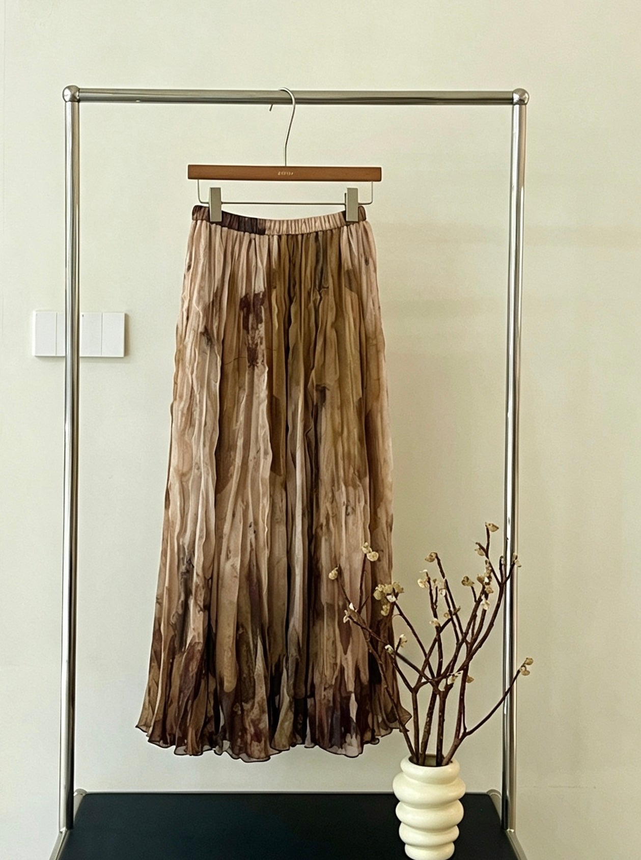 Khaki tie-dye print pleated flowy skirt hanging on a rack