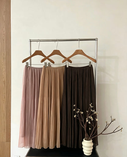 Pleated maxi skirts in pink, apricot, and dark brown hanging on a rack